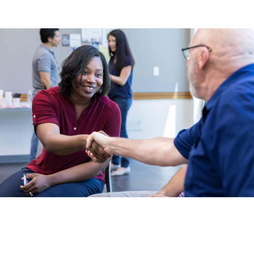 A smiling woman shaking hands with a seated man in a community setting